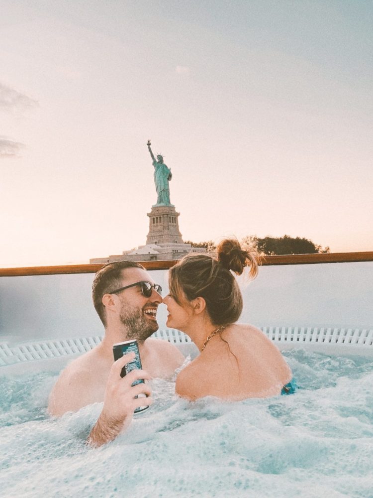 Engaged couple in hot tub boat looking at statue of liberty