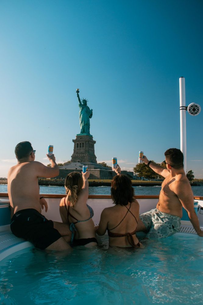 group of people in a hot tub boat looking at statue of liberty in NYC