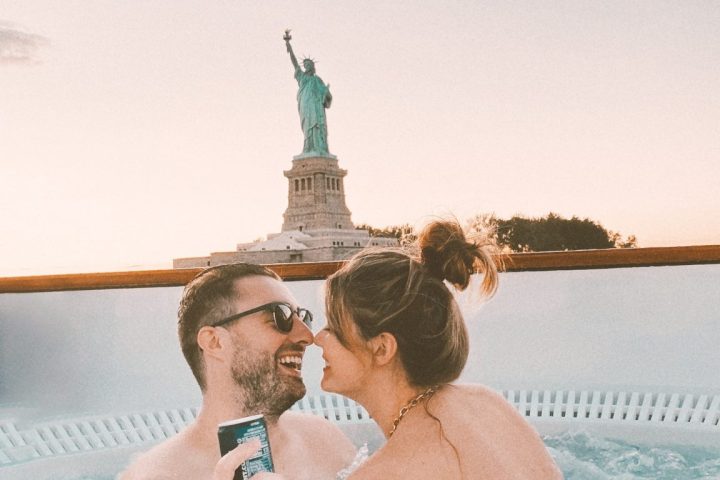 Engaged couple in hot tub boat looking at statue of liberty