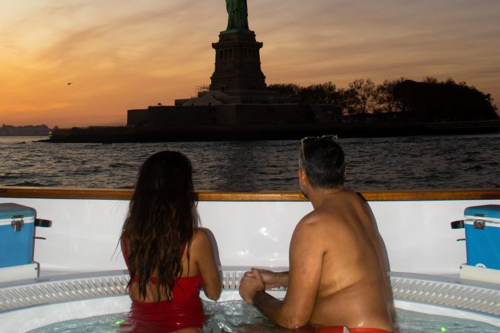 couple in hot tub boat looking at statue of liberty