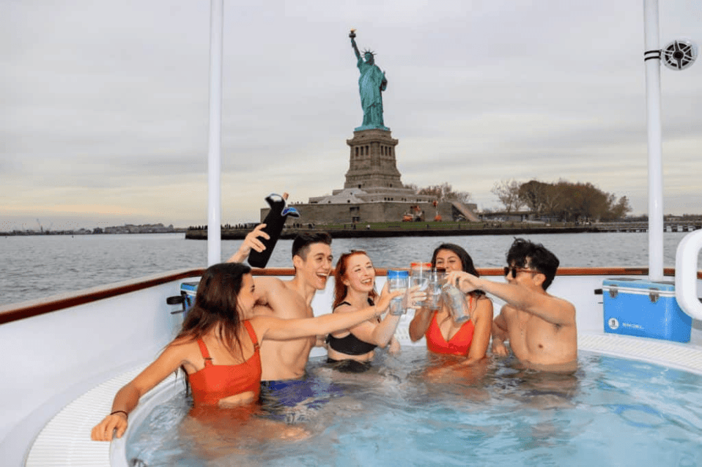people in hot tub boat in front of statue of liberty