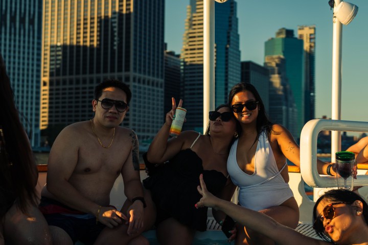 Group of people on a boat enjoying drinks with city skyline in the background.