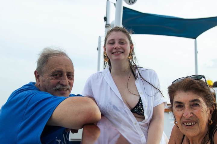 Three people smiling on a boat deck with blue sunshades overhead.